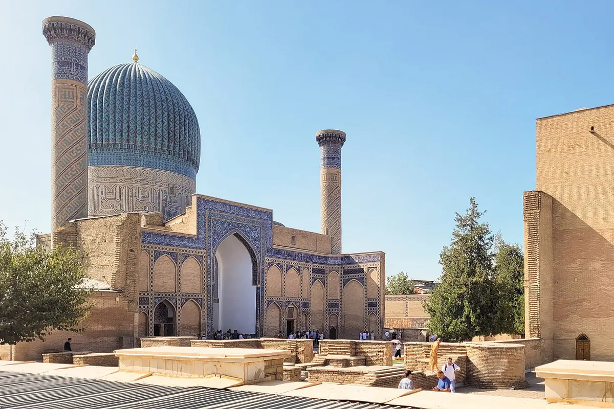 The ribbed blue dome and minaret of the Gur-e-Amir mausoleum in Samarkand beside a tall brick portal